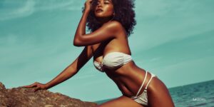 young woman posing against a rock in front of her at the beach after a tummy tuck procedure